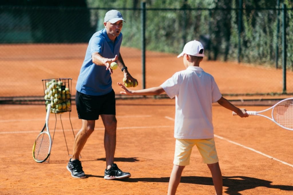 Tennis Instructor with Young Talent on Clay Court. Boy having a Tennis Lesson.