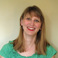 Woman smiling wearing green top standing against a neutral background
