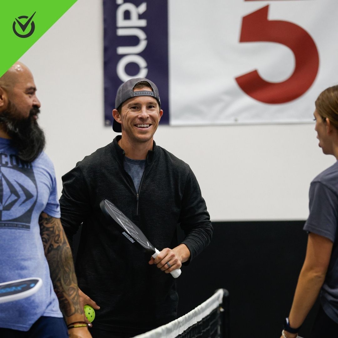 Photo of two pickleball players laughing on an indoor court
