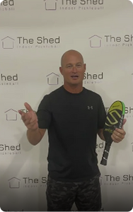 Man holding pickleball paddle in front of the shed indoor pickleball backdrop