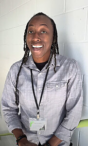 Person smiling wearing a light button-up shirt and name badge with braided hair