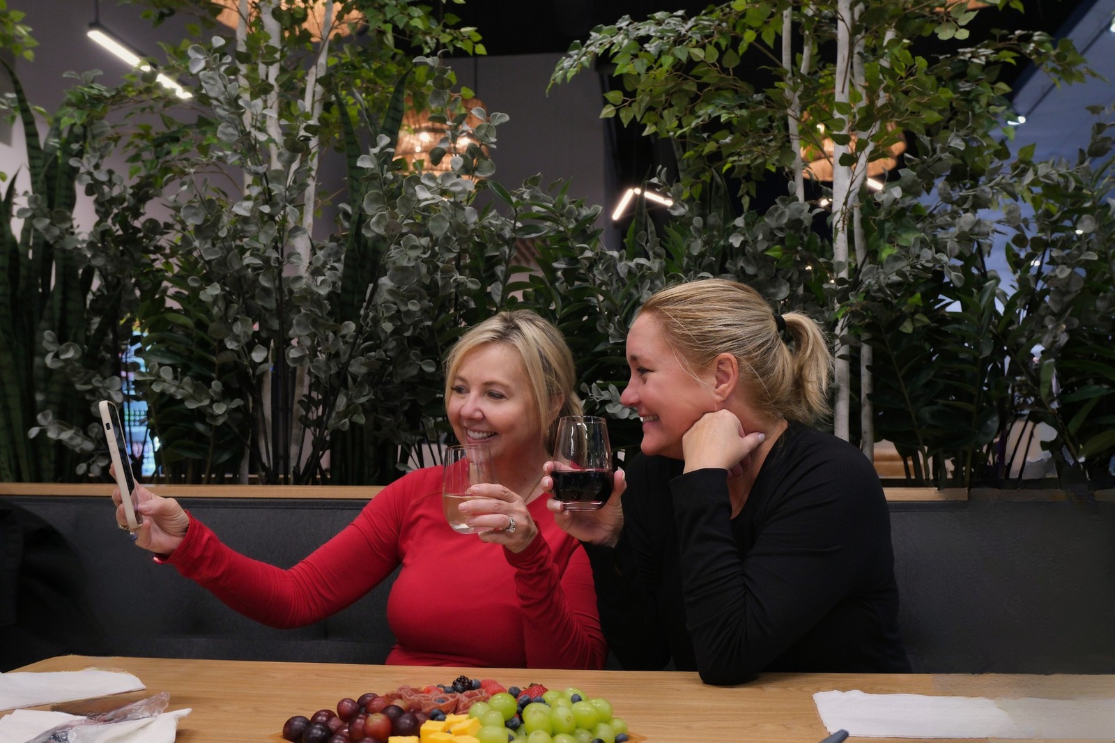 Two women hold up their drinks and take a selfie in Pickleball Zone's bar area