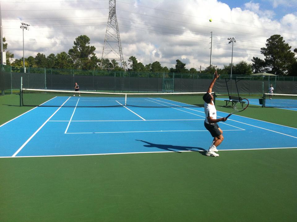 Tennis player serving on bright blue court at Lake Cane Tennis Center