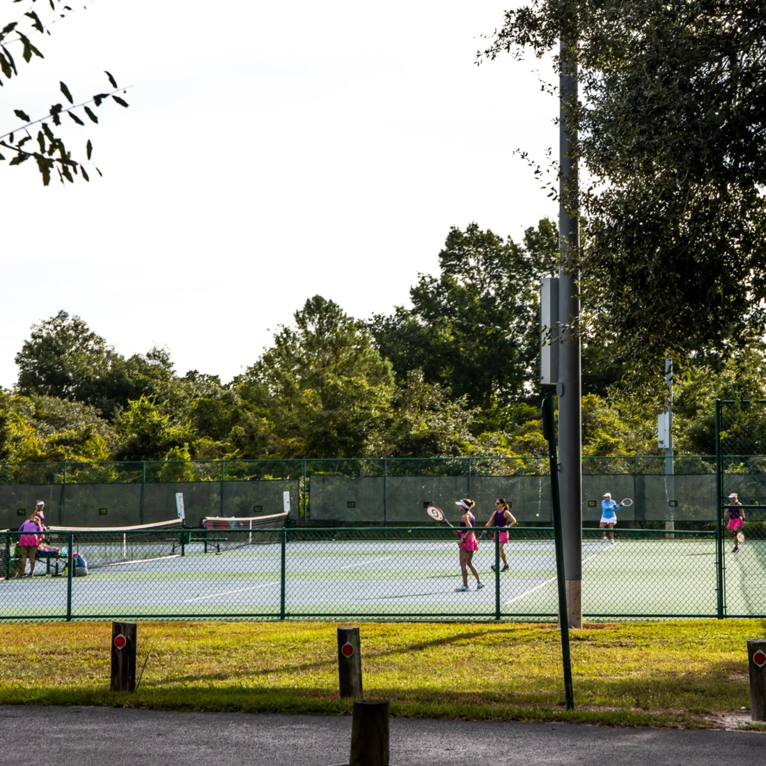 People playing tennis on an outdoor court surrounded by trees