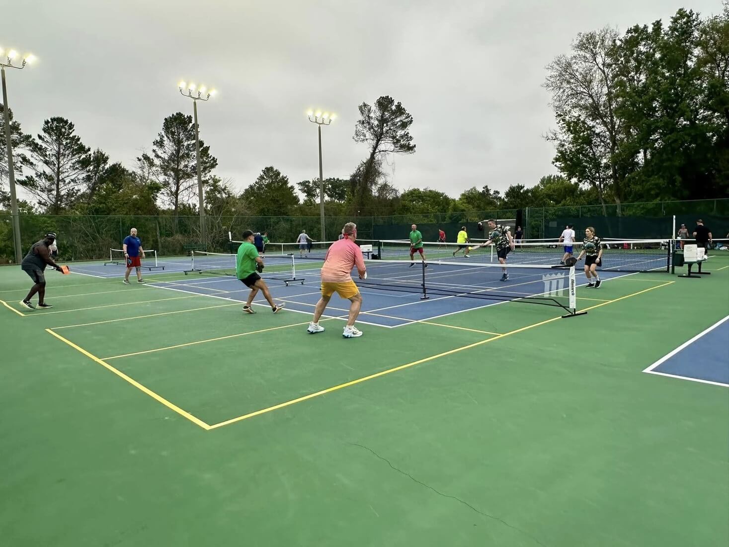 Multiple people playing pickeball on outdoor courts under lights