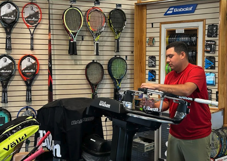 Staff member stringing a tennis racket inside the Lake Cane Tennis Center pro shop