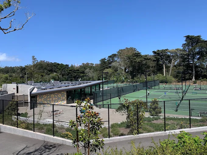 Outdoor tennis facility with modern clubhouse and multiple courts surrounded by trees.