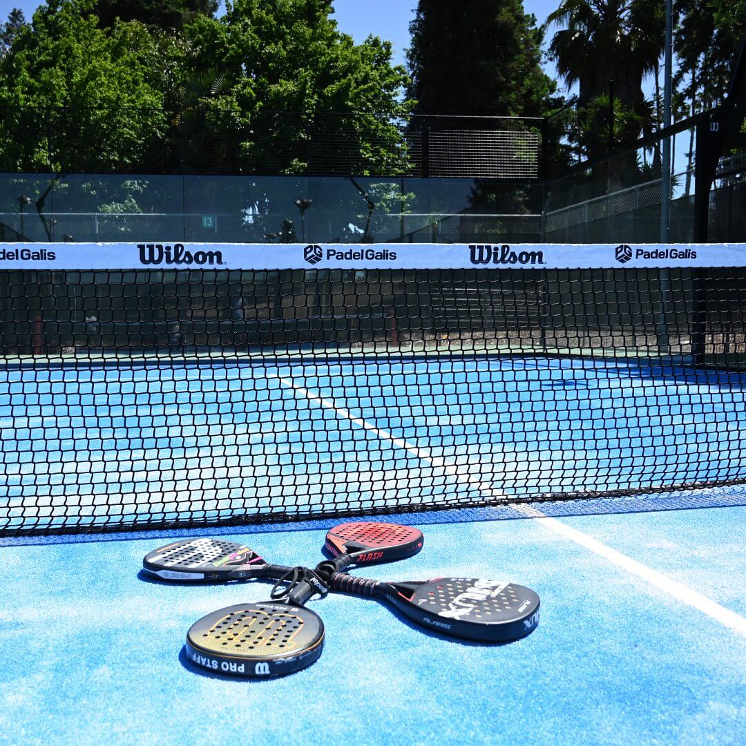 Close-up of padel rackets placed on the ground near the net.