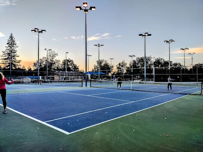 Players practicing tennis on outdoor courts under evening lights.
