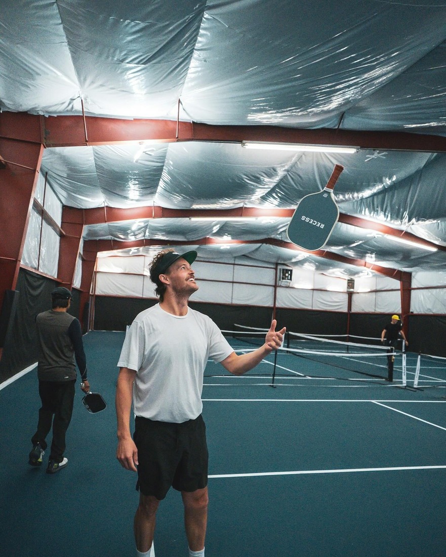 A player smiles while tossing a pickleball paddle in the air on one of Bozeman Classic’s indoor courts.