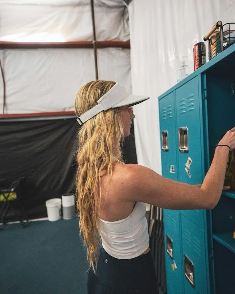 A woman wearing a visor and athletic wear stores equipment inside blue lockers at Bozeman Classic Pickleball Club.