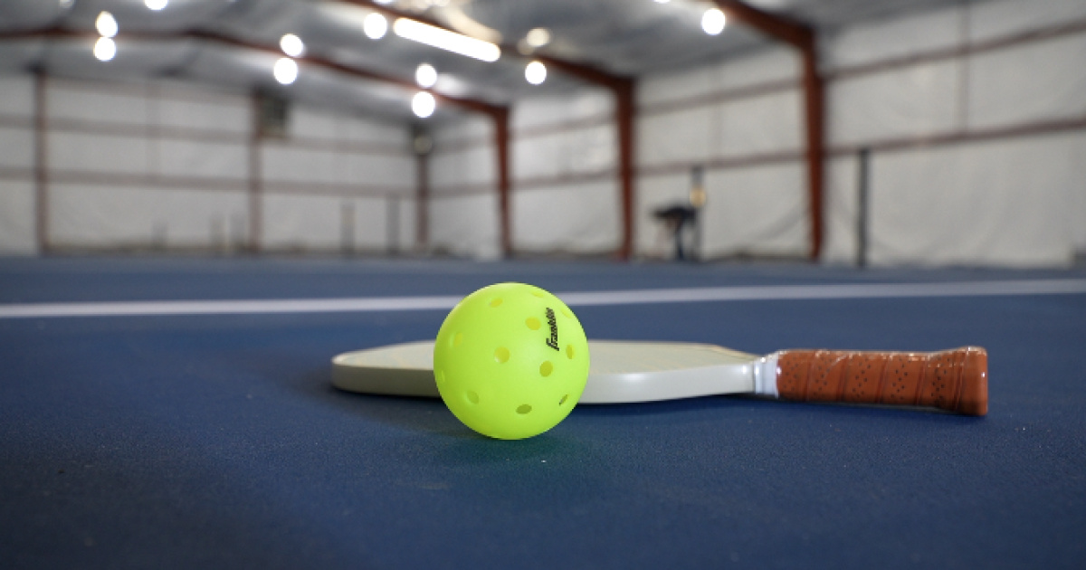 A bright yellow pickleball and paddle resting on an indoor court at Bozeman Classic Pickleball Club.