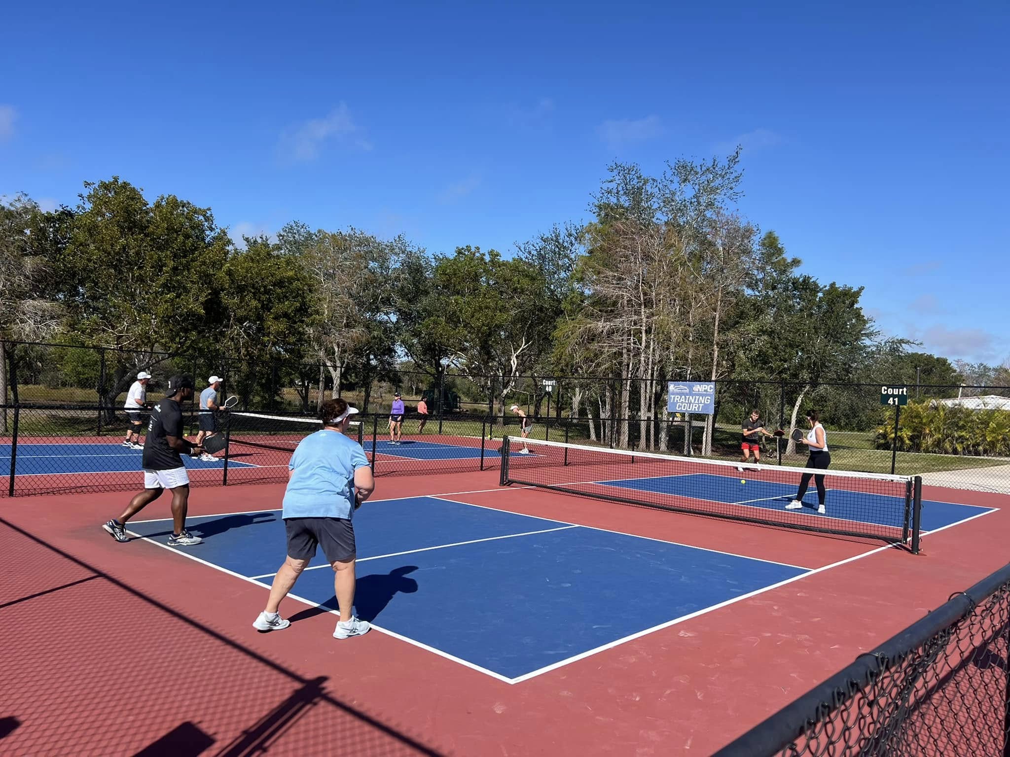 Players competing in doubles matches on blue and red outdoor pickleball courts.