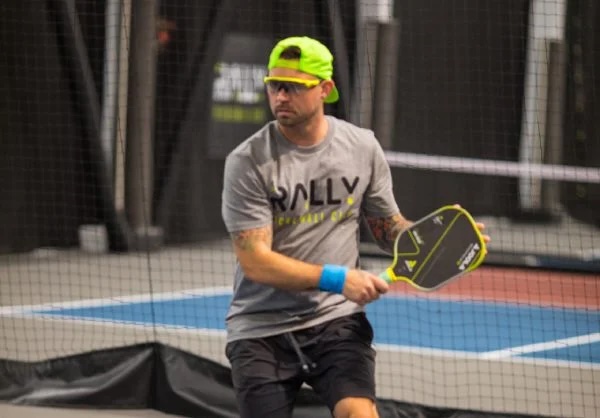 A male pickleball player in a Rally Pickleball Club shirt mid-shot on an indoor court in Auburn, Washington.