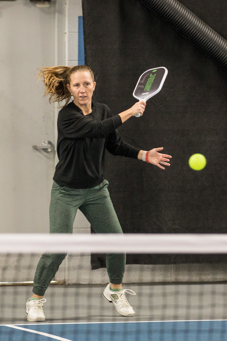 A female pickleball player mid-swing at Rally Pickleball Club in Auburn, Washington, playing on an indoor cushioned court.