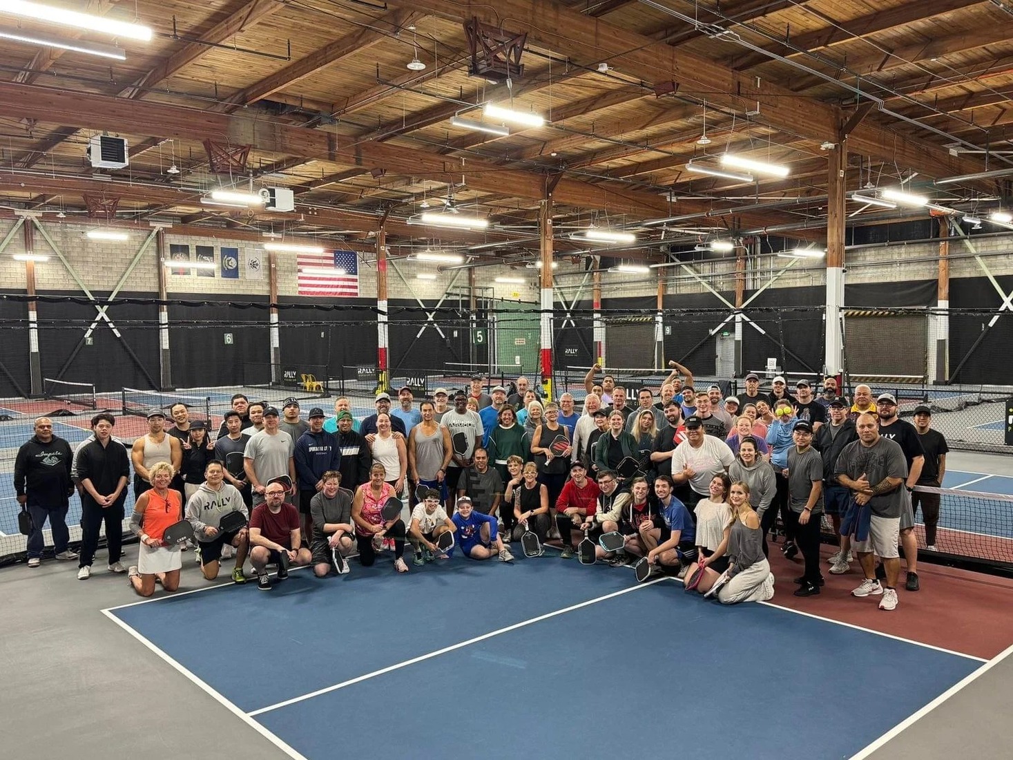A large group of Rally Pickleball Club members and players gathered on the indoor courts in Auburn, Washington, with the American flag visible in the background.