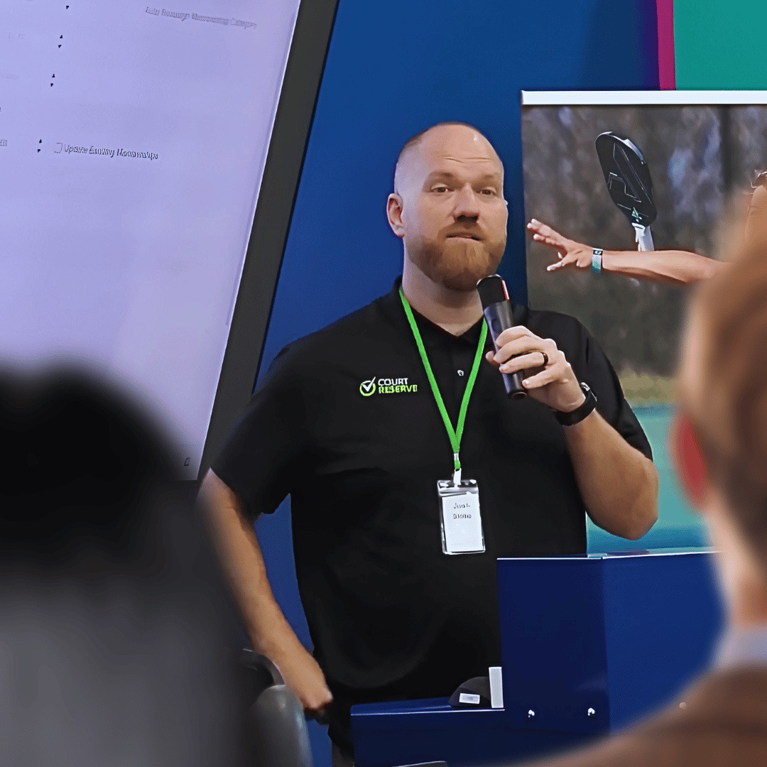 Photo of a male CourtReserve Academy instructor speaking to a crowded room with microphone in hand